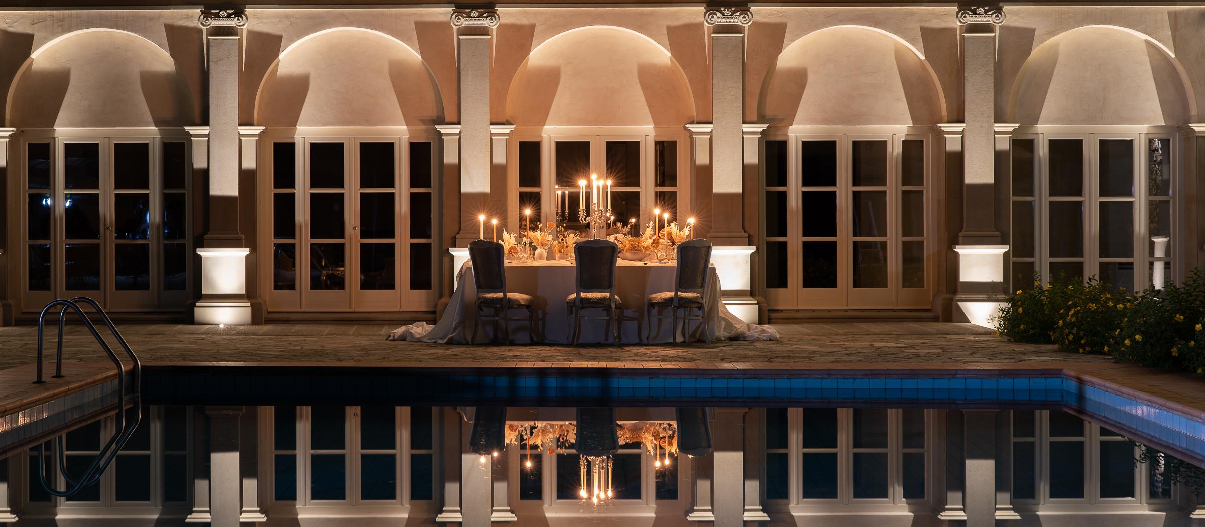 Elegant outdoor wedding dinner with candlelit table reflected in the pool
